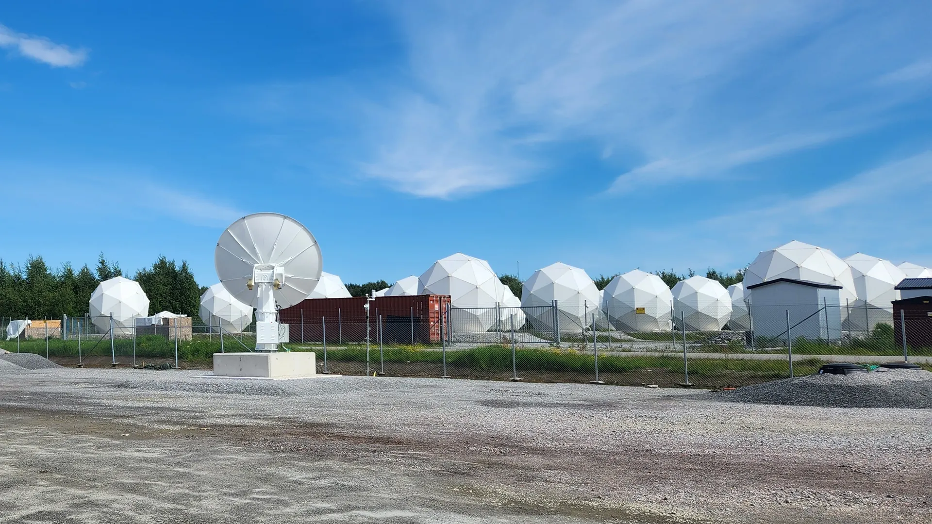 Tracking antenna and a row of radomes on the fenced Arctic Space Center site, Piteå.